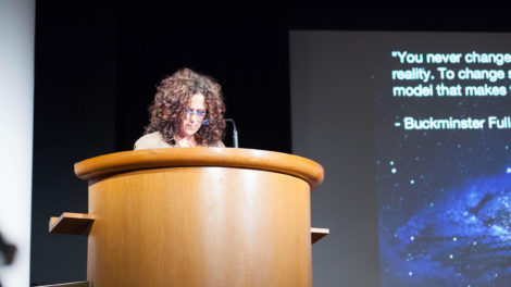 Jacki Sumell at a podium on the stage of the Peter B. Lewis Theater